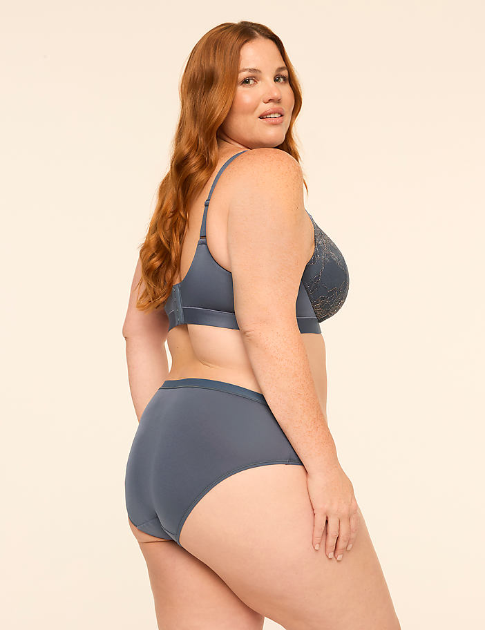 A woman with long red hair wearing a blue lingerie set poses against a plain, light-colored background.