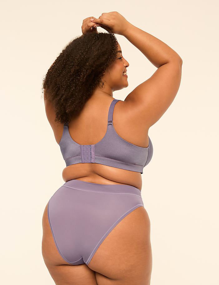 A woman with curly hair wearing a purple lingerie set poses against a plain, light-colored background.