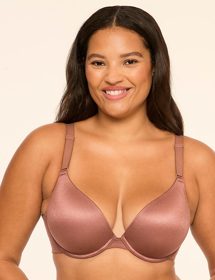 A smiling woman wearing a shimmering mauve bra stands against a plain, light-colored background.