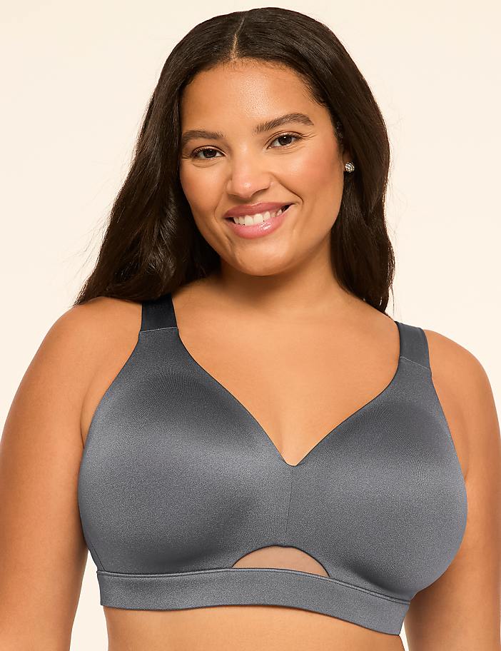 A smiling woman with long dark hair wears a grey bra against a plain, light-colored background.