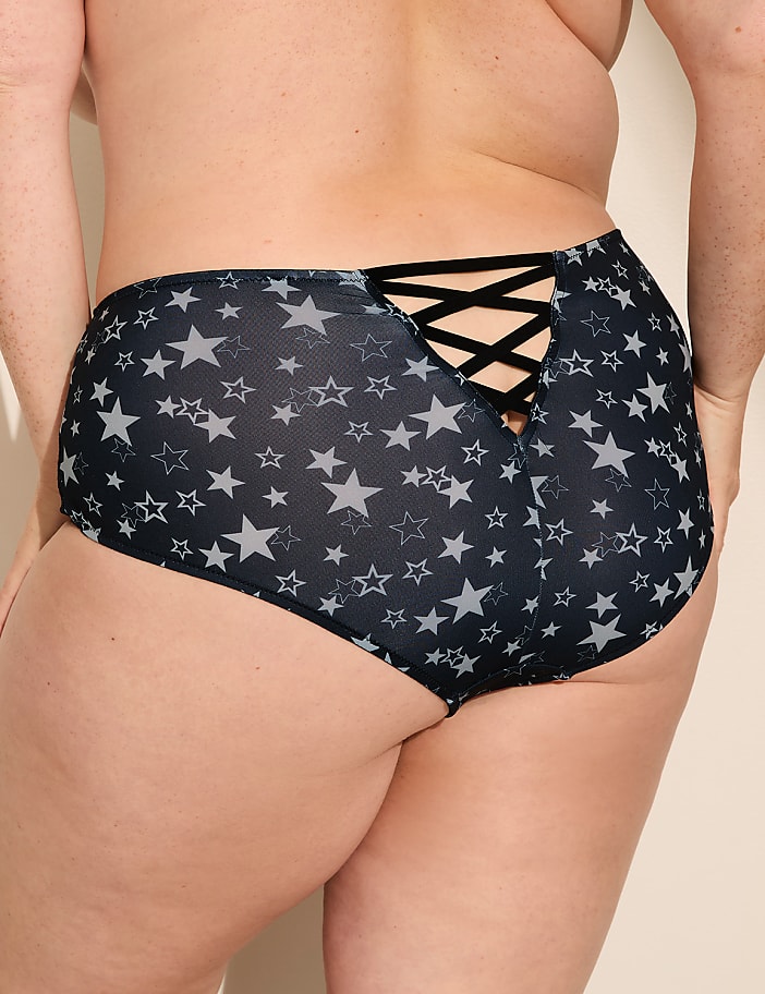 A person wears navy blue star-patterned bottoms with a criss-cross strap detail against a plain, light-colored background.