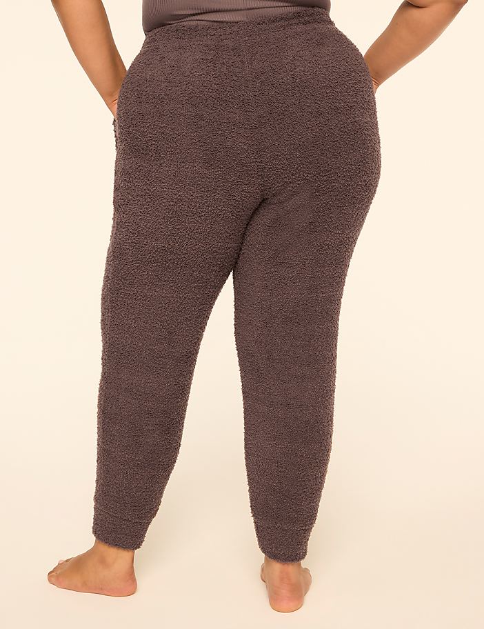 A person stands with their back to the camera wearing dark purple fuzzy pants against a plain, light-colored background.