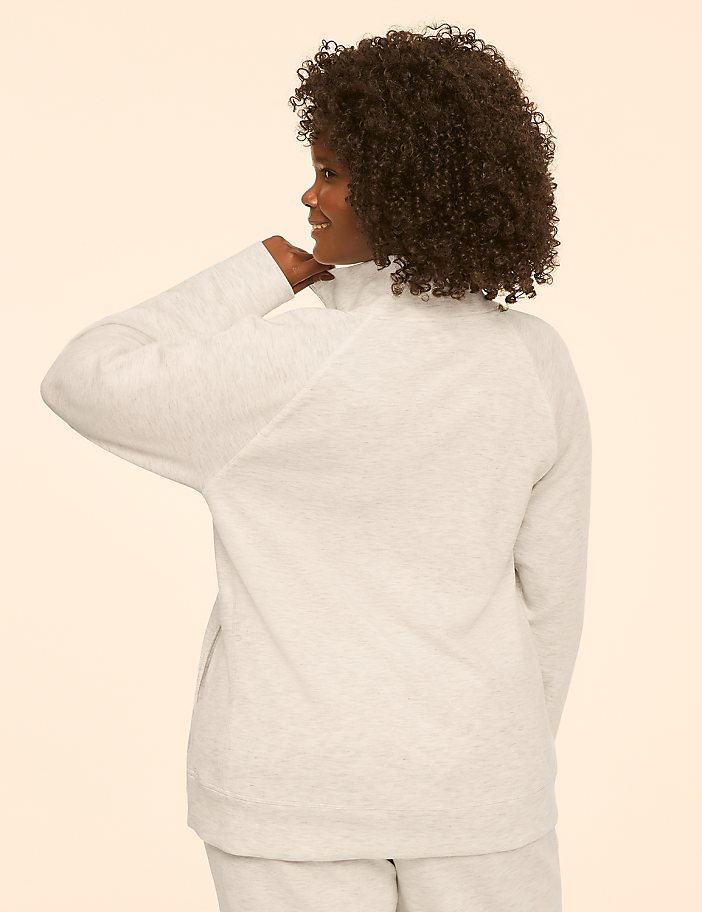 A woman in a light-colored sweater and pants stands against a plain, light-colored background.