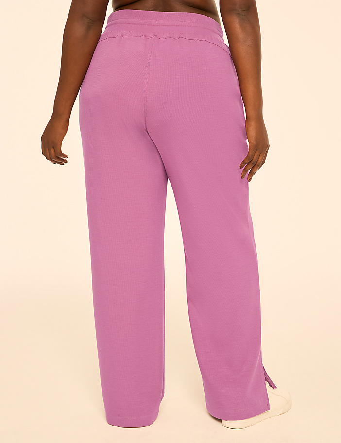 A person wearing pink ribbed wide-leg pants stands against a plain cream background.