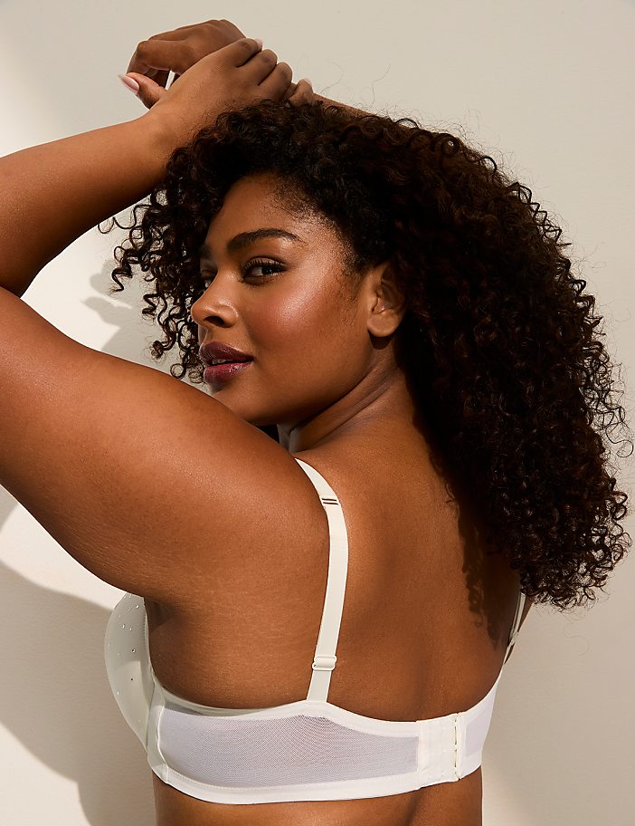 A woman with curly dark hair wearing a white bra poses against a plain white background.