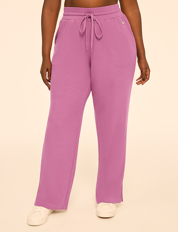 A person wearing rose-colored sweatpants with white sneakers stands against a plain, light-colored background.