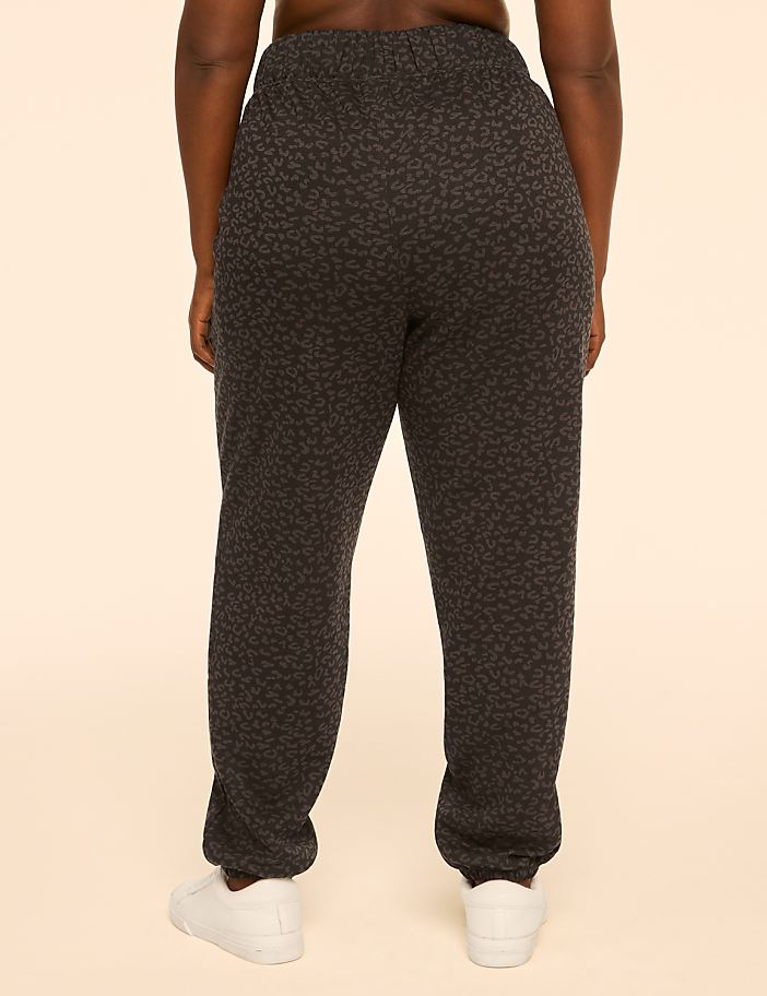 A person wearing patterned sweatpants and white sneakers stands against a plain, light-colored background.