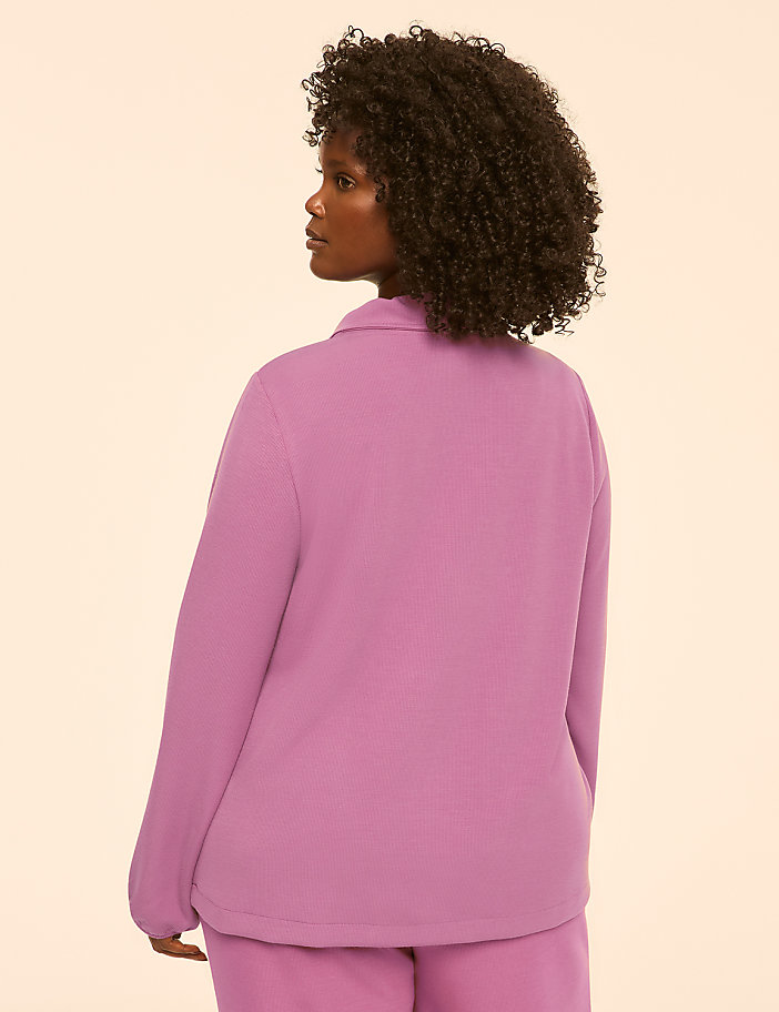 A woman in a pink collared shirt and pants stands against a plain, light-colored background.