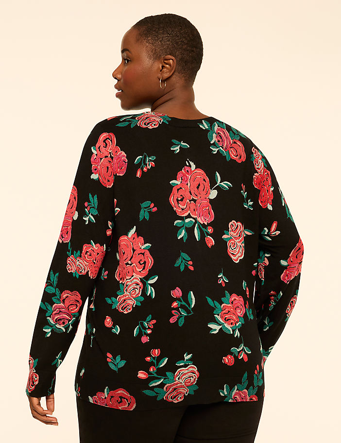 A woman wearing a black floral print top stands against a plain, light-colored background.