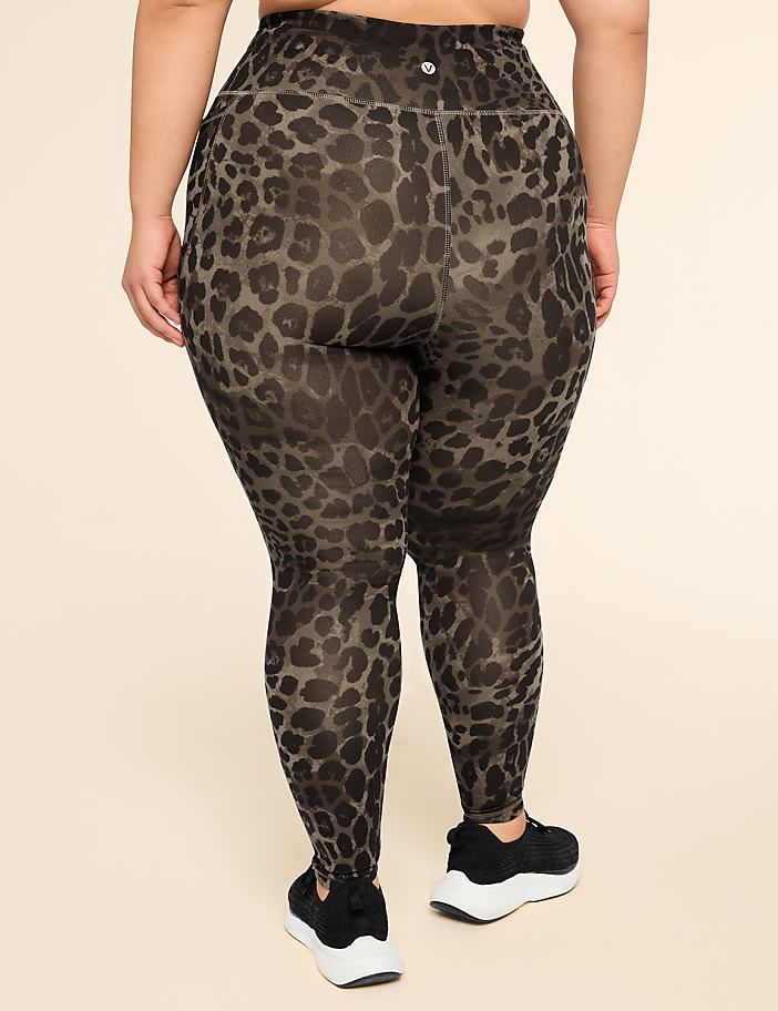 A person wearing leopard print leggings and black sneakers stands against a plain, light-colored background.