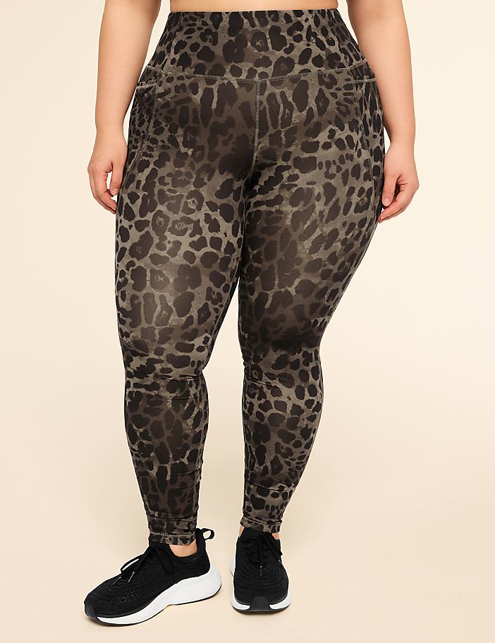 A person wearing leopard-print leggings and black sneakers stands against a plain, light-colored background.
