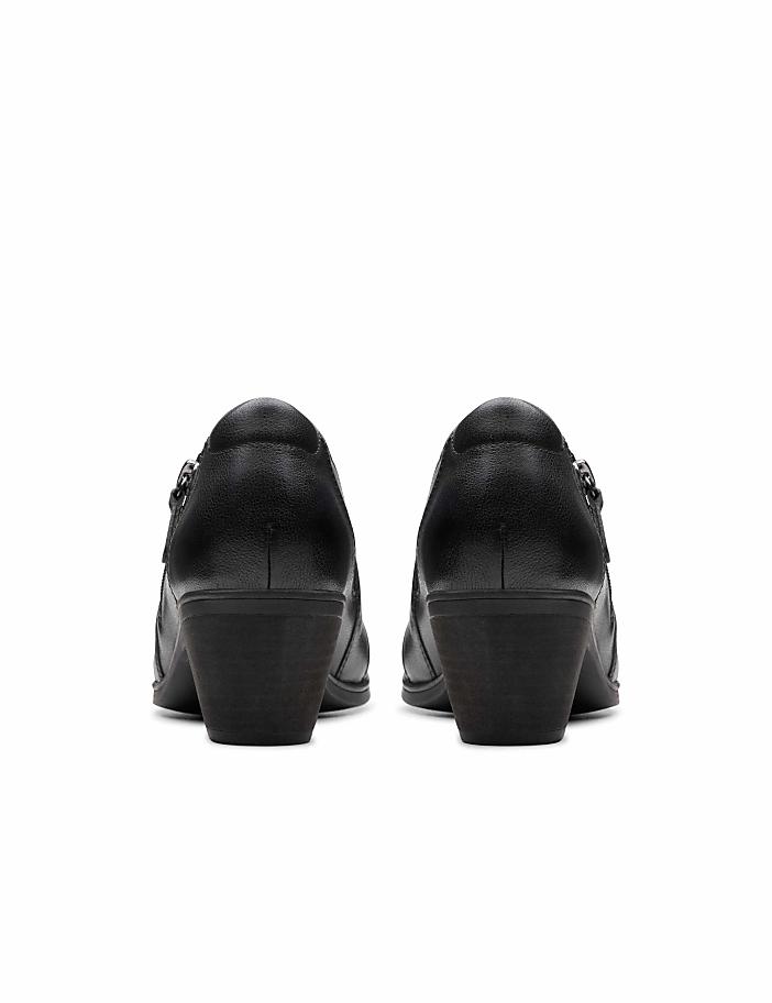 A pair of black leather heeled shoes are positioned in the foreground against a plain white background.