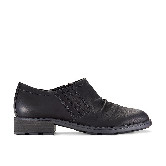A single black leather shoe sits in the foreground against a plain white background.