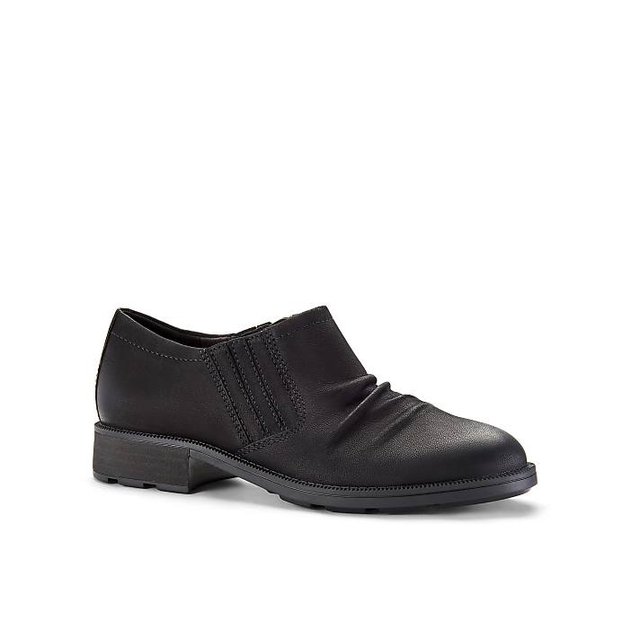 A single black leather shoe sits in the foreground against a plain white background.