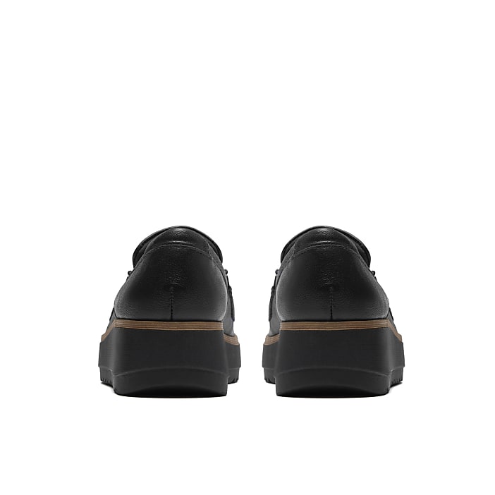 A pair of black leather platform shoes is positioned in the foreground against a plain white background.