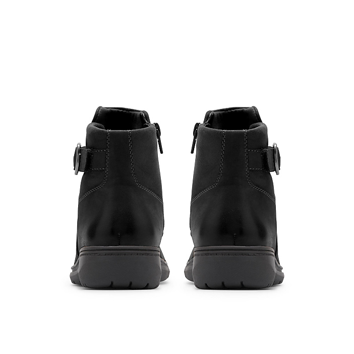 A pair of black ankle boots is positioned in the foreground against a plain white background.