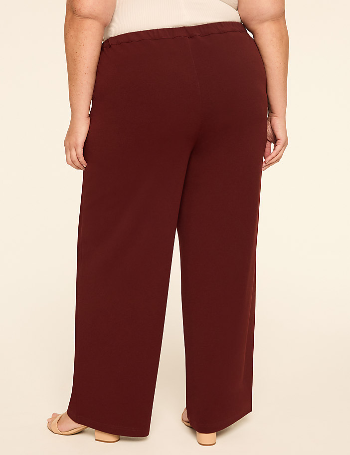 A person wearing brown wide-leg pants and black heels stands against a plain, light-colored background.