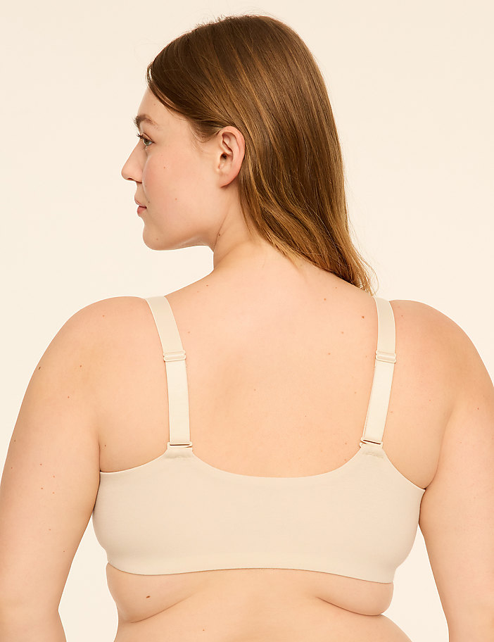 A woman in beige undergarments stands with her back to the viewer against a plain, light-colored background.