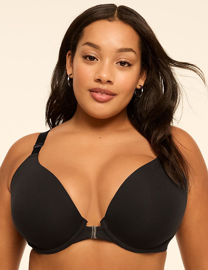 A woman with dark hair and freckles poses in a black bra against a plain, light background.