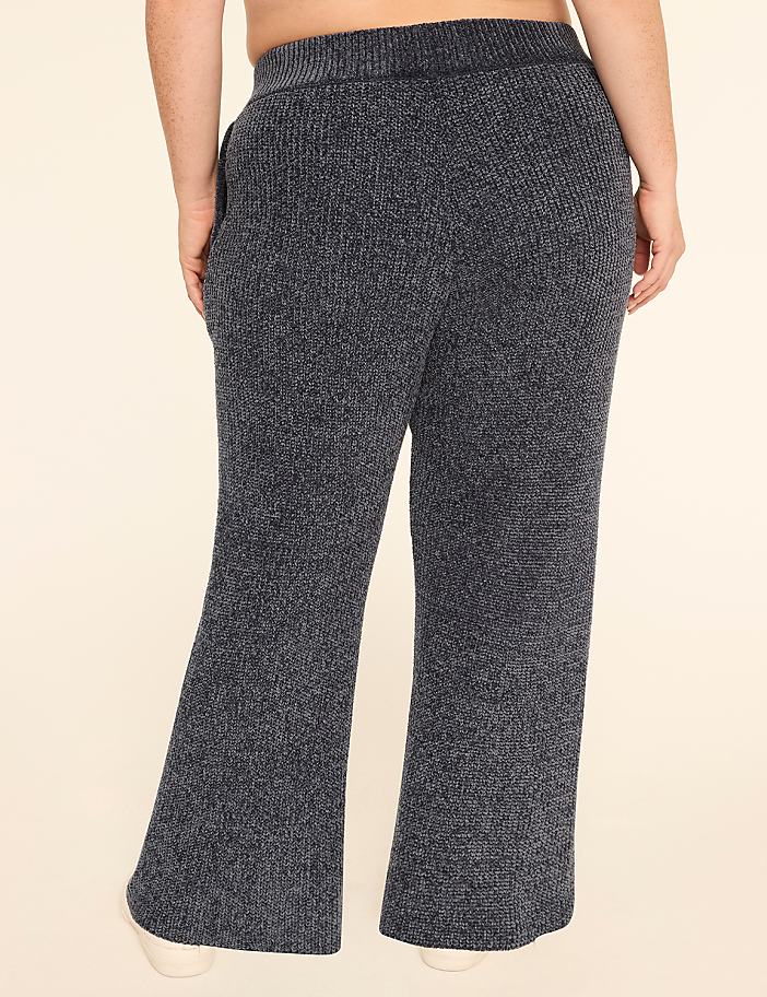A person wearing fuzzy dark gray lounge pants stands against a plain cream background.