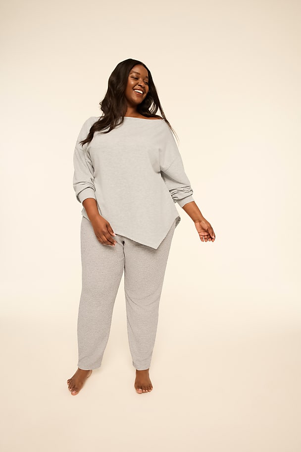 A smiling woman wearing a grey long-sleeved top and matching striped pants stands against a plain, light-colored background.
