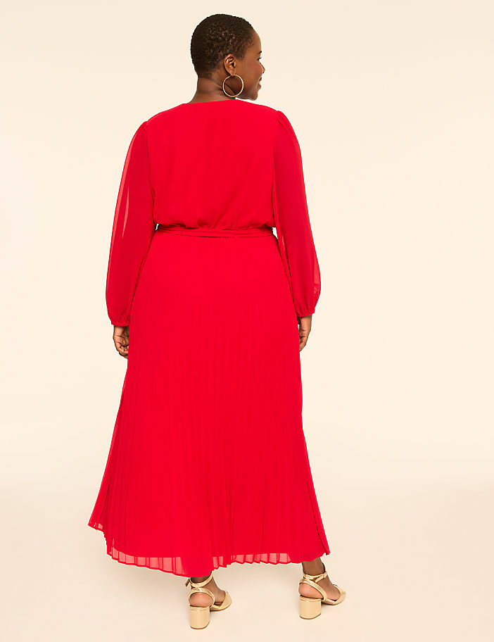 A woman in a red dress stands against a plain, light-colored background.