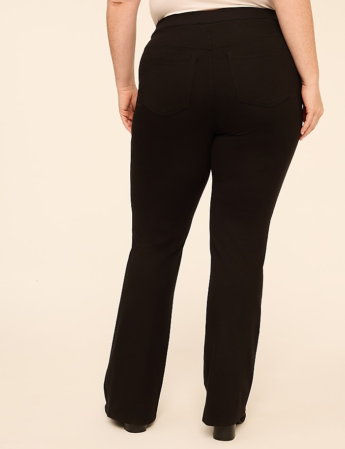 A person wearing black flared trousers stands against a plain, light-colored background.