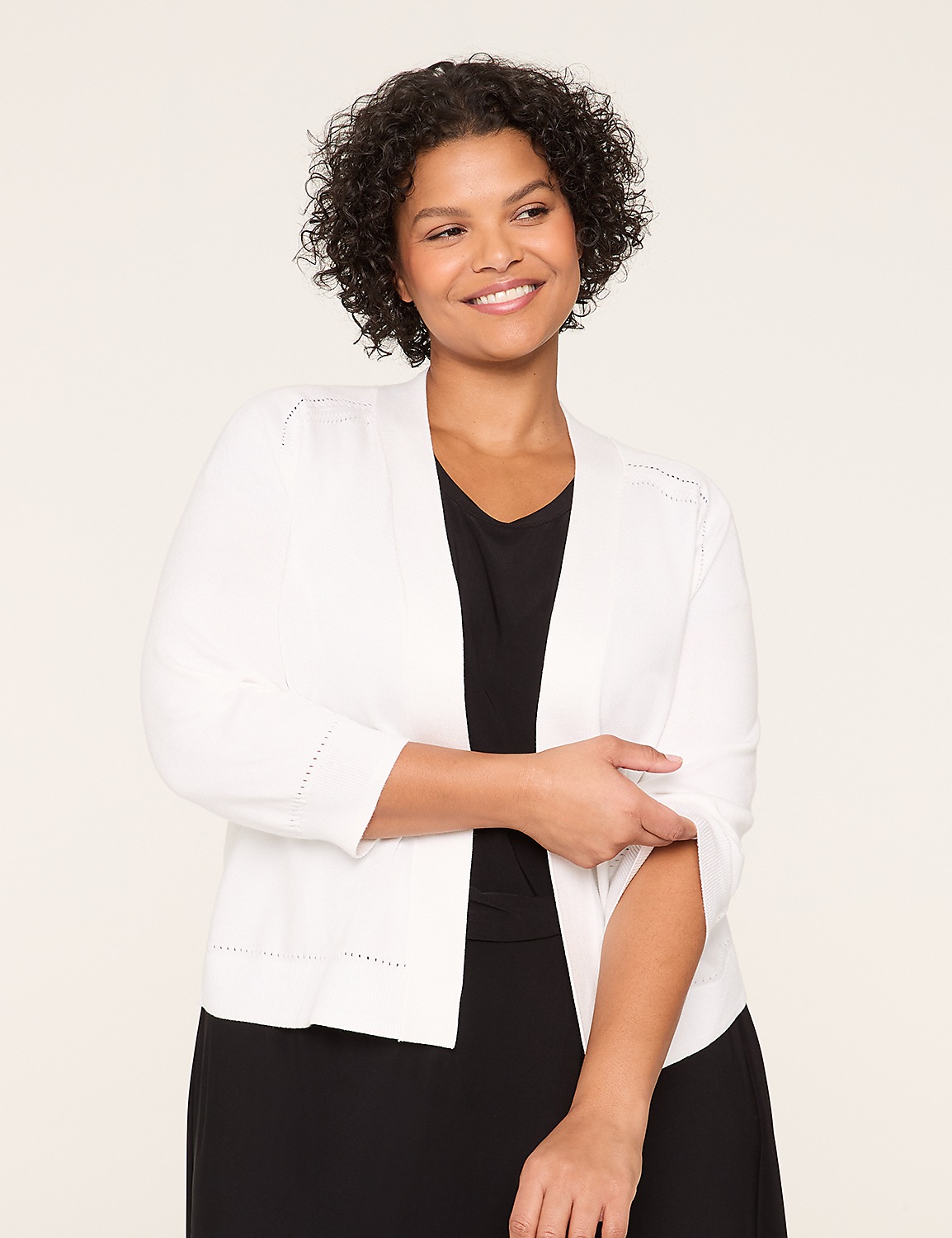 A smiling woman with curly hair wearing a white jacket and black top stands against a plain white background. Product Image 1