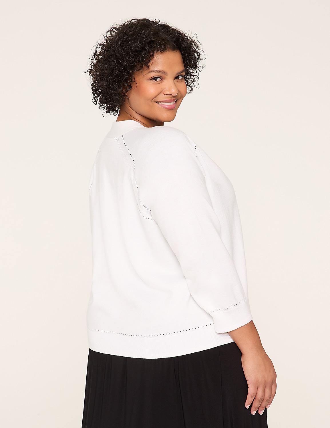 A smiling young woman with curly dark hair wearing a white sweater stands against a plain light-colored background. Product Image 2