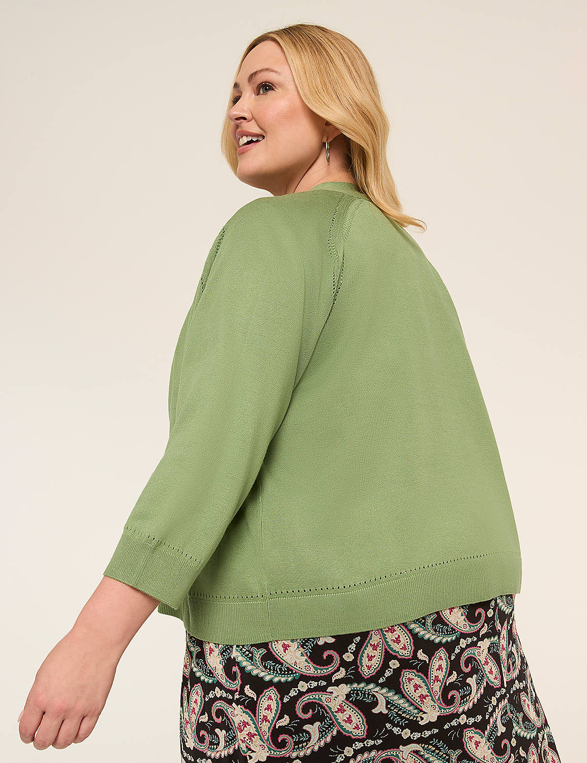A smiling woman with blonde hair wearing a green top and a patterned skirt stands against a plain background. Product Image 2