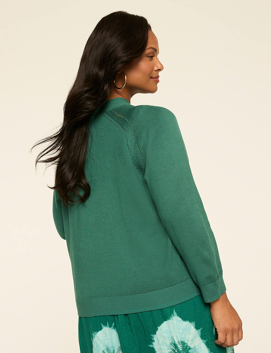 A woman with long, dark hair wearing a green sweater stands against a plain, light-colored background. Product Image 2