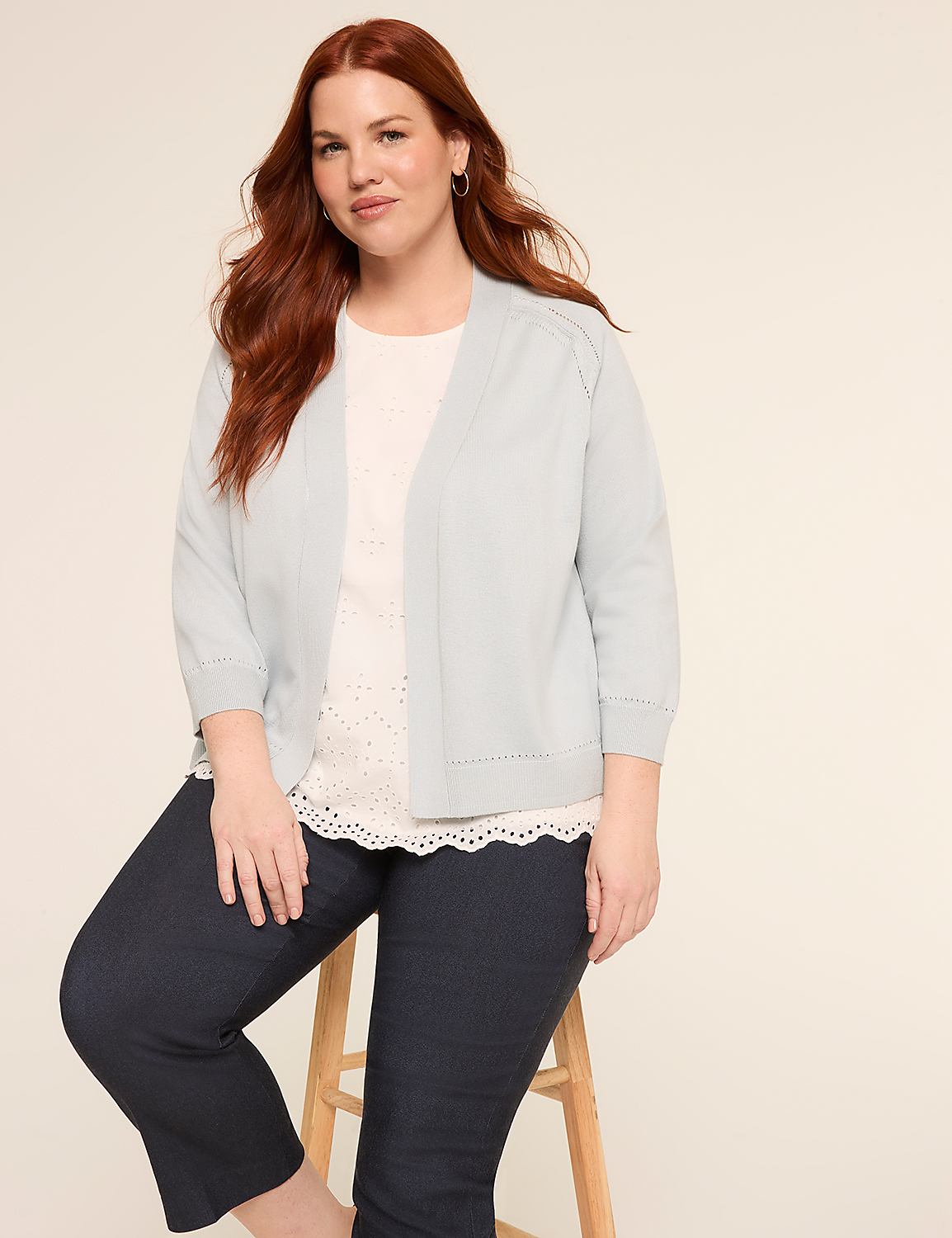 The image shows a woman with long, reddish-brown hair wearing a white top and a gray cardigan, sitting on a wooden stool against a plain beige background. Product Image 3