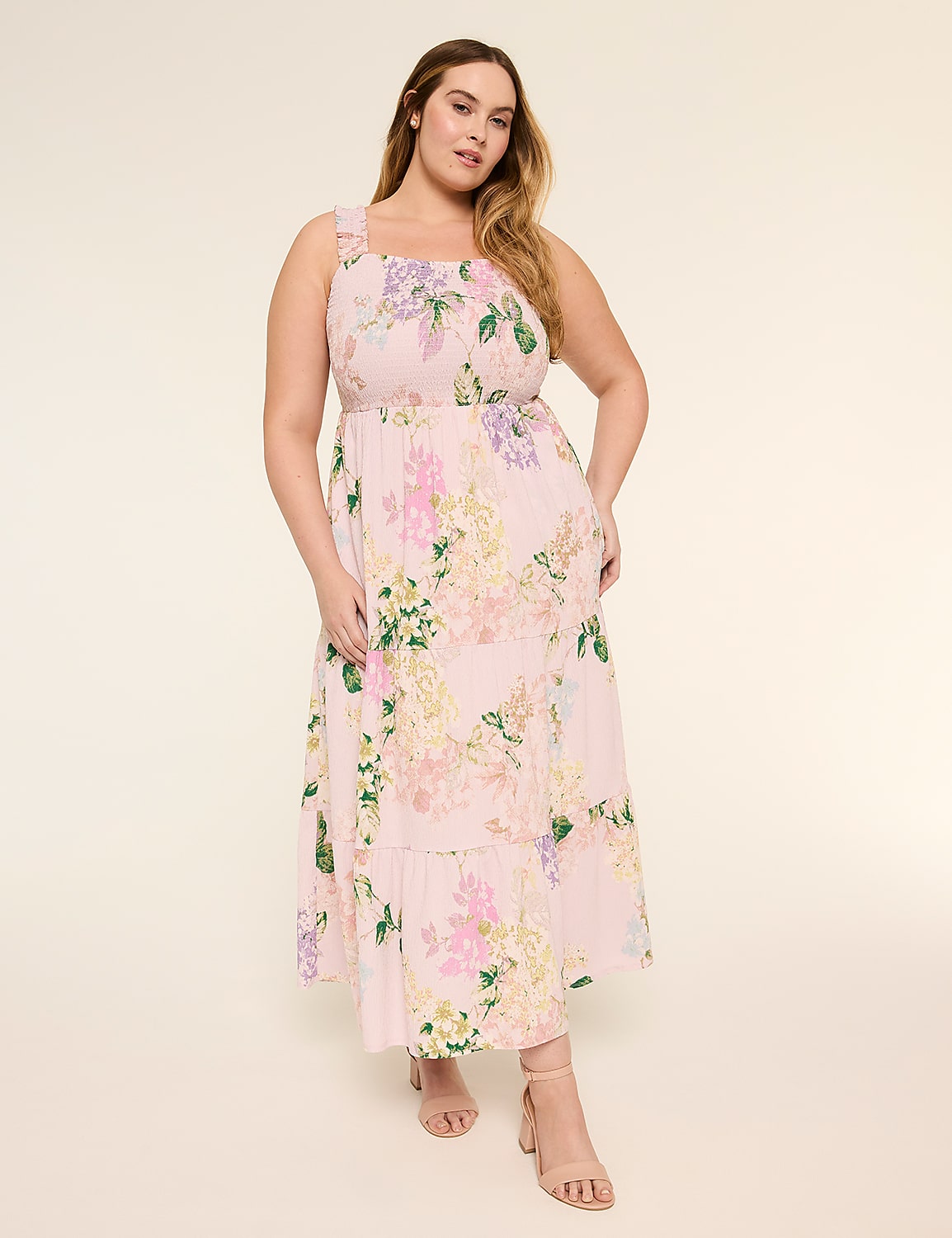 A young woman wearing a floral print dress stands in a neutral-colored background, her long hair flowing and a warm, friendly expression on her face. Product Image 1