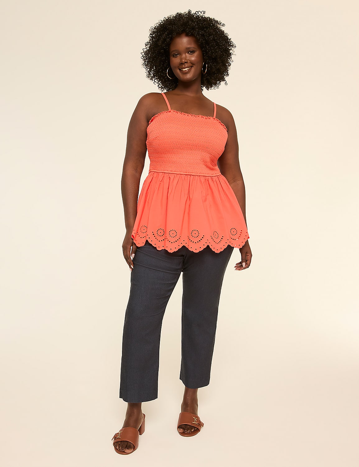 A smiling woman with curly hair wearing a bright orange top and black pants stands against a plain background. Product Image 3