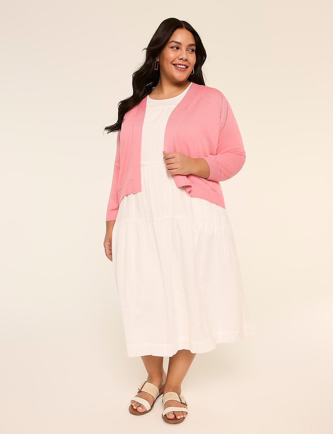 A smiling woman wearing a pink cardigan and a white dress stands against a plain beige background. Product Image 3