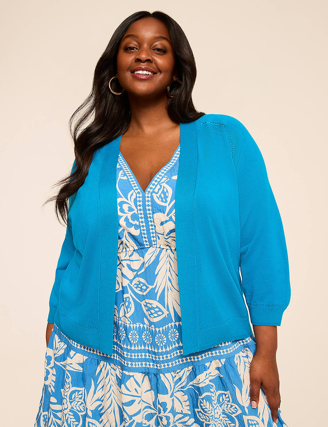 A smiling woman with long dark hair wearing a bright blue top and a patterned dress stands against a plain beige background. Product Image 1
