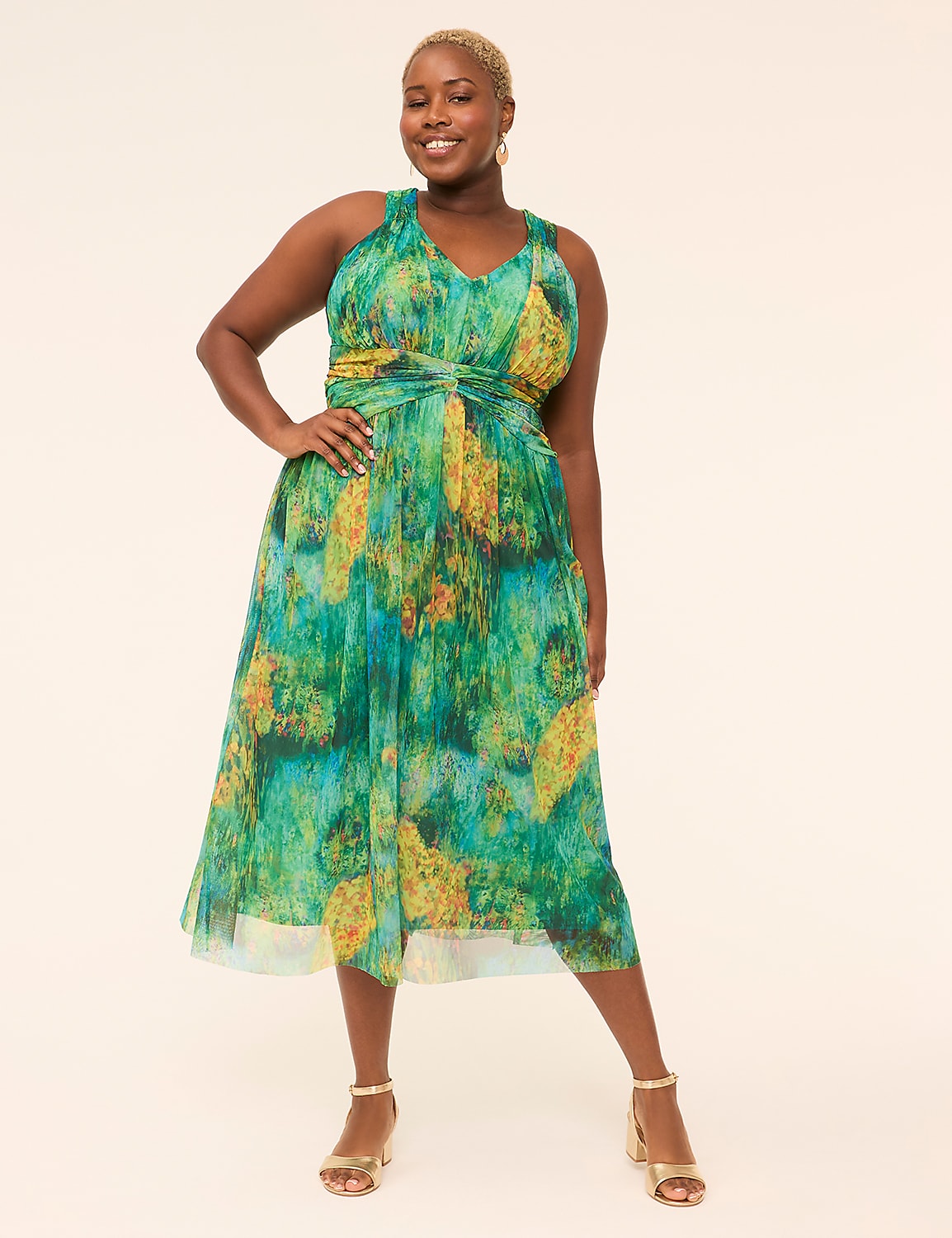 A smiling woman in a green and yellow abstract print dress stands against a plain, light-colored background. Product Image 1