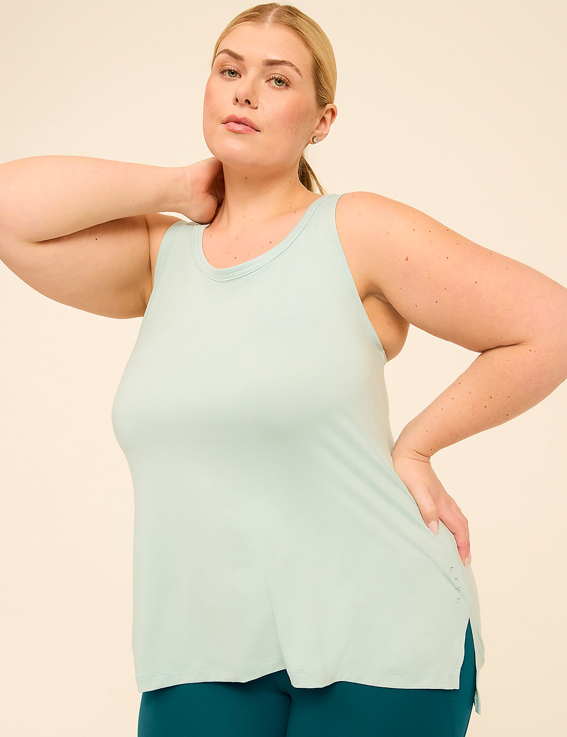 A woman in a light blue tank top and teal leggings poses against a plain beige background. Product Image 1