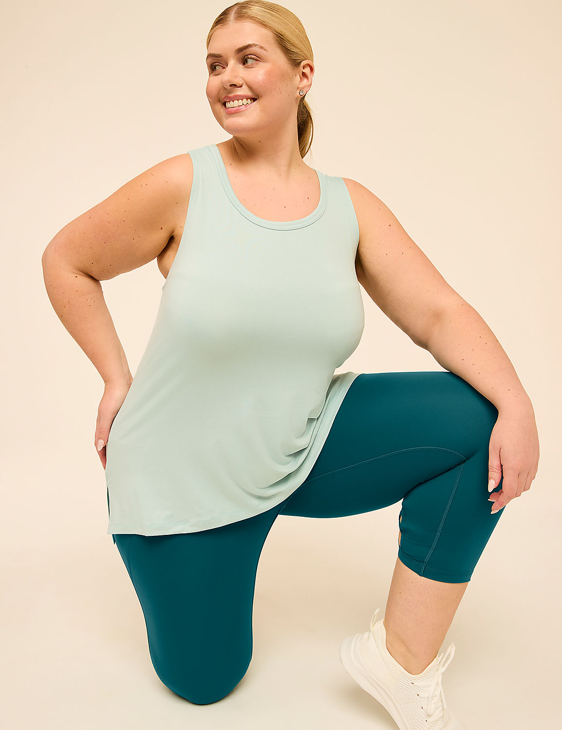 A woman in a light blue tank top and teal capri leggings kneels on a plain beige background. Product Image 3