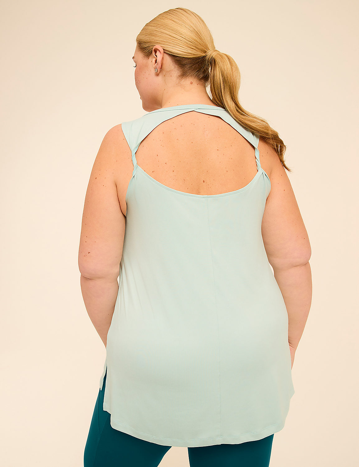 A woman in a light green tank top with a cutout back and teal leggings stands against a plain beige background. Product Image 2