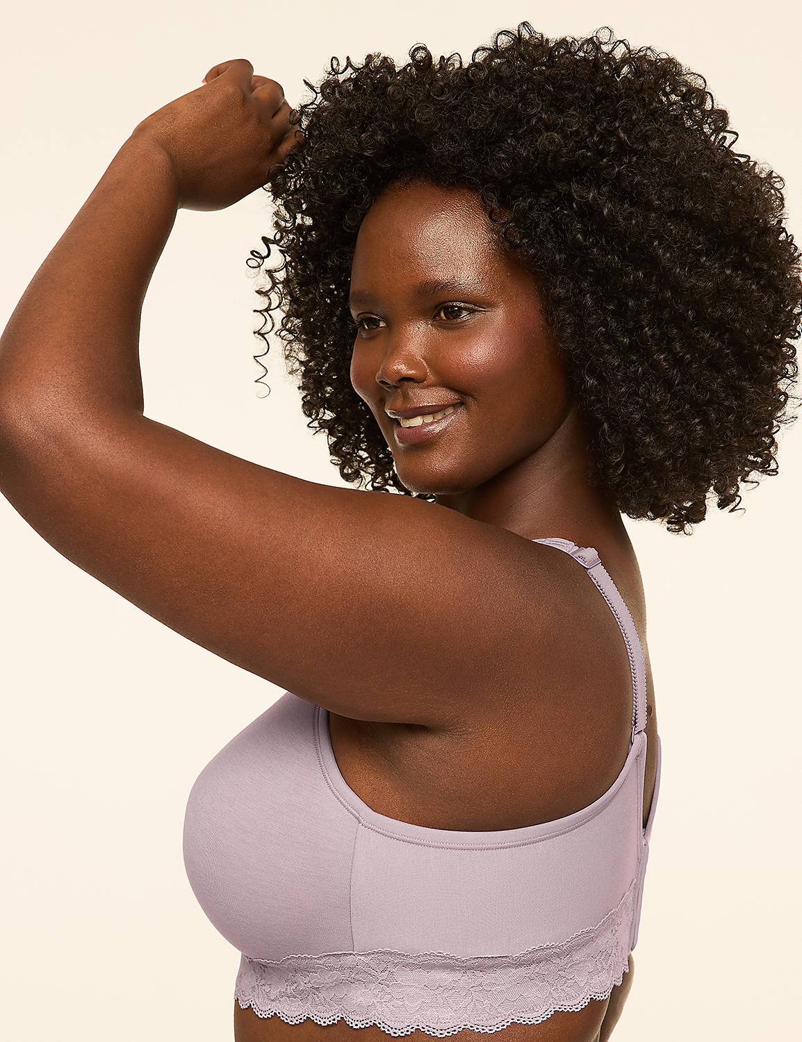 A woman with dark, curly hair smiles as she adjusts her arm, wearing a light purple bra with lace trim against a plain, light background. Product Image 3