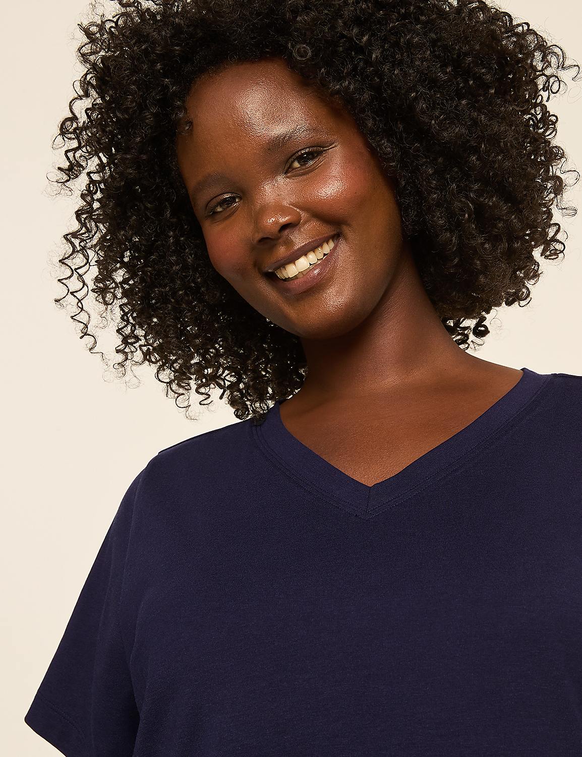 A smiling woman with curly dark hair wears a navy blue v-neck shirt against a plain, light-colored background. Product Image 4
