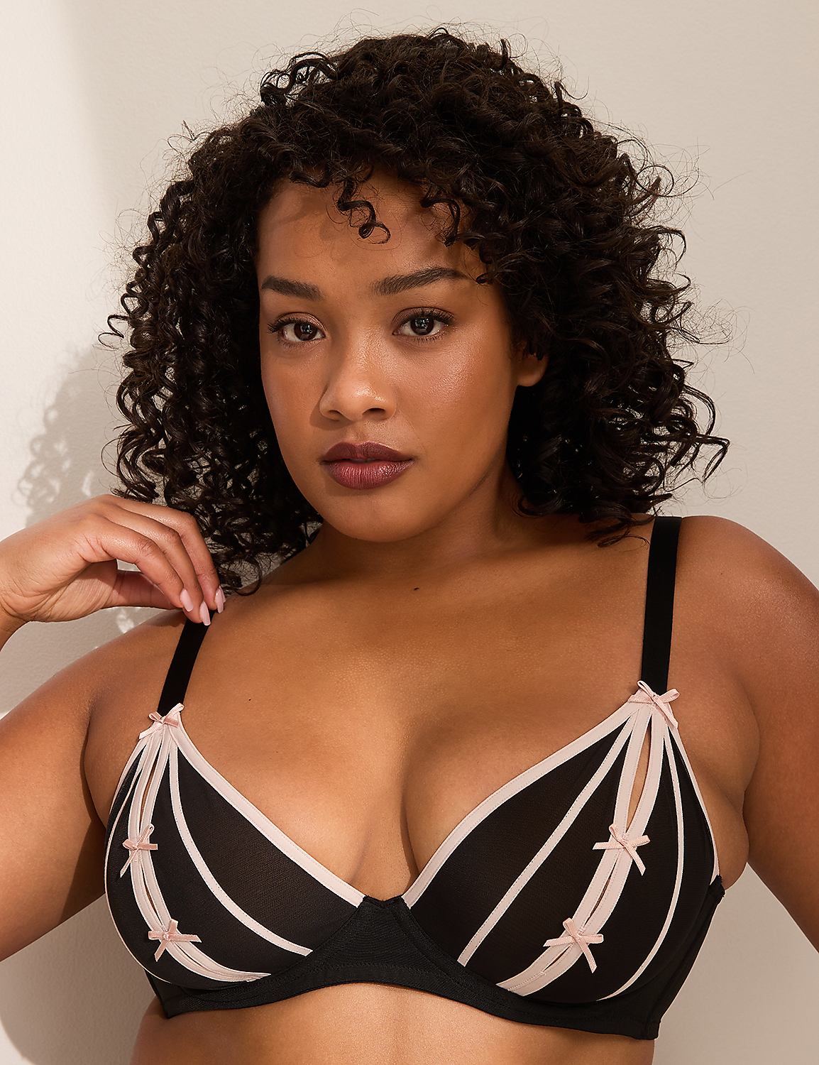 A woman with curly dark hair wears a black and pink bra, with a plain light background. Product Image 1