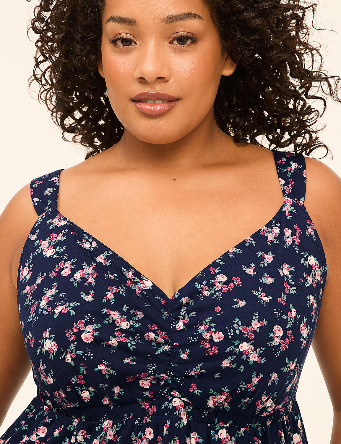 A woman with curly dark hair smiles gently in a navy floral dress against a plain, light background. Product Image 3