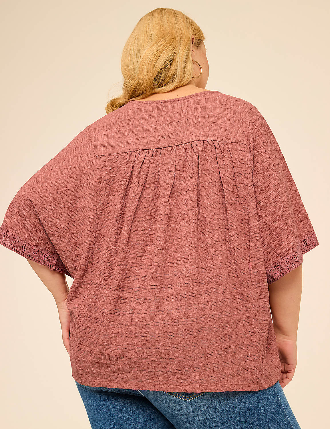 A woman in a textured rose-colored top with lace trim on the sleeves stands against a plain, light brown background. Product Image 2