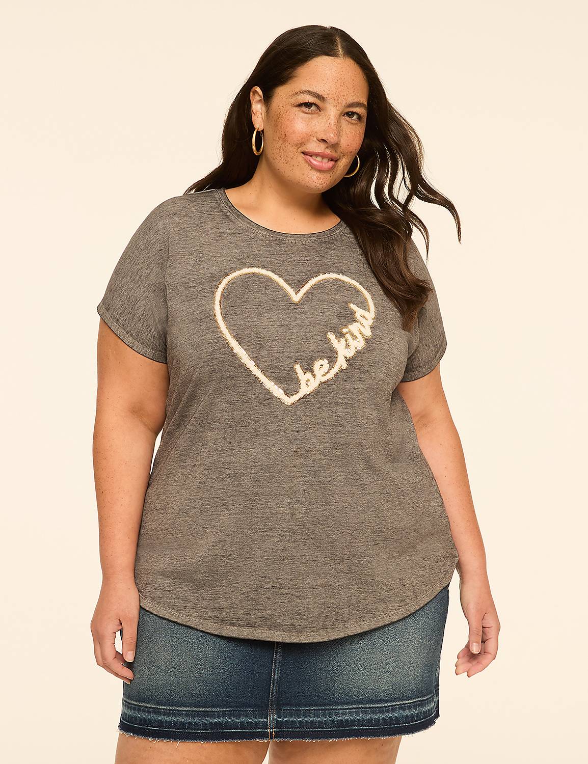A woman in a grey t-shirt with a heart design and a denim skirt stands against a plain, light-colored background. Product Image 1