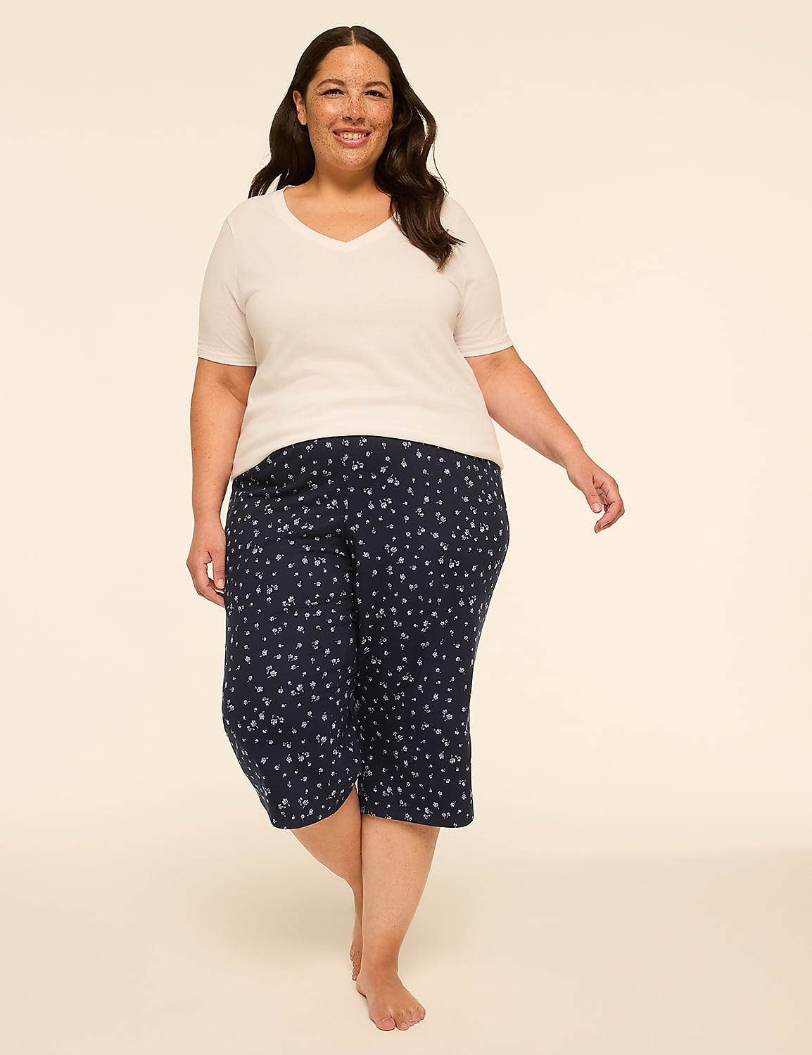 A smiling woman in a white v-neck shirt and navy floral capri pajamas stands against a plain, light beige background. Product Image 3