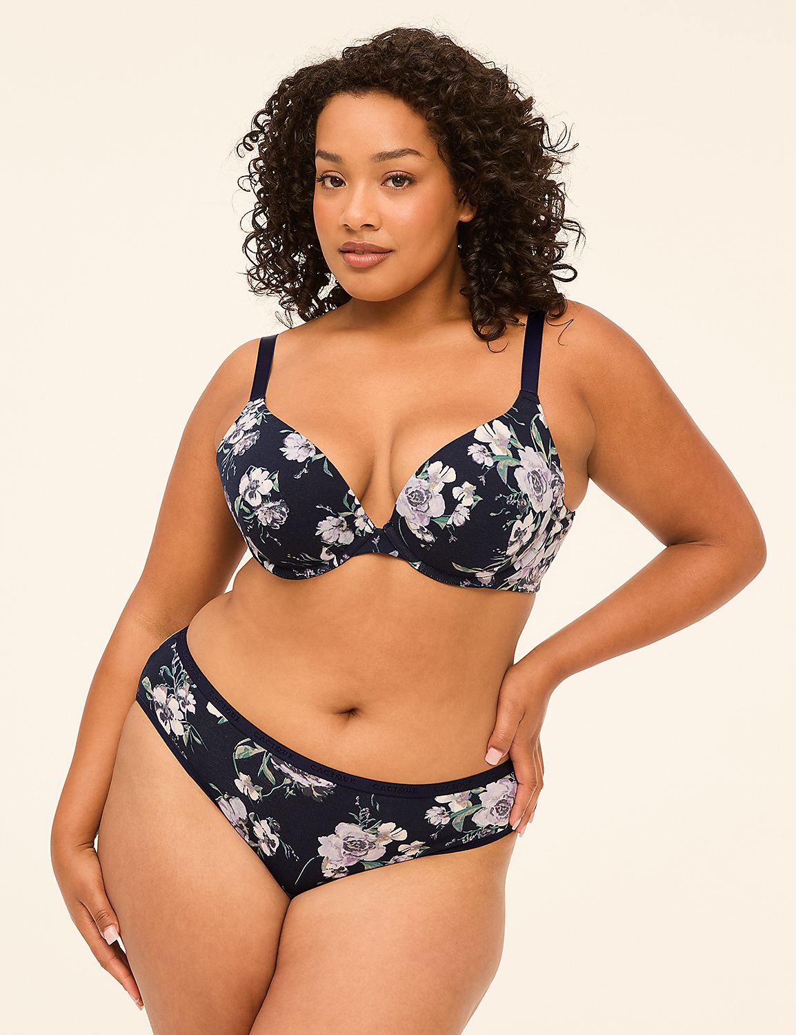 A woman with curly dark hair poses in a floral navy blue bra and matching underwear against a plain, light-colored background. Product Image 4