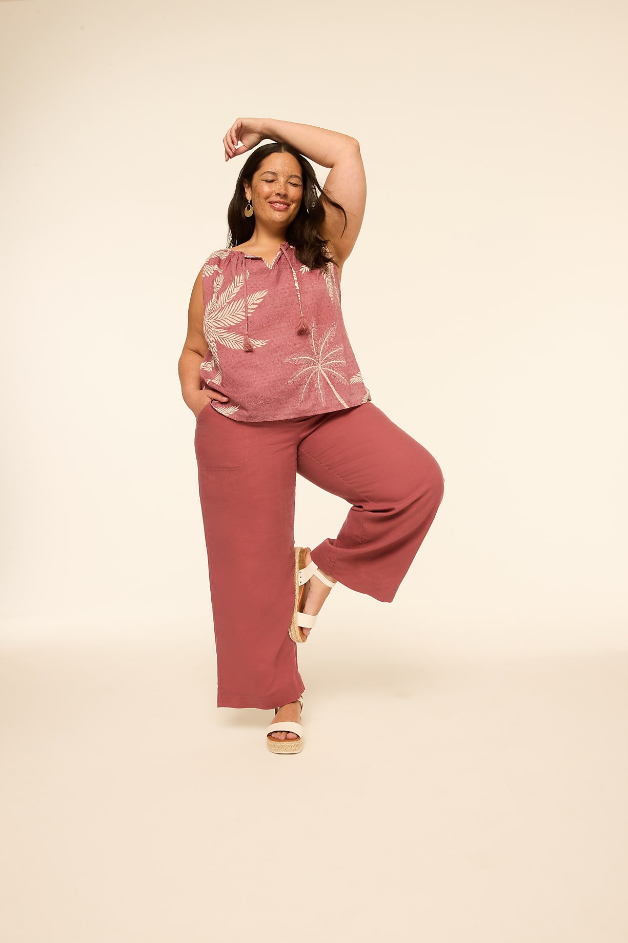 A smiling woman in a pink floral top and wide-leg pants stands against a plain, light-colored background. Product Image 4
