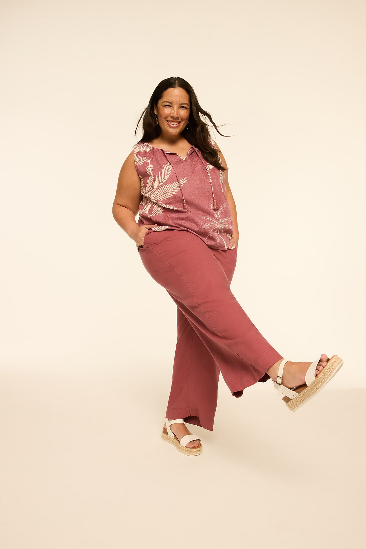 A smiling woman in a floral top and pink pants poses against a plain, light-colored background. Product Image 5